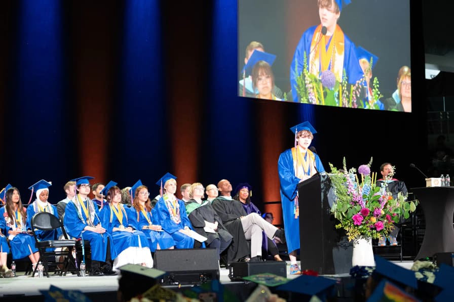 Nick Oates on stage at his high school graduation, giving a speech.